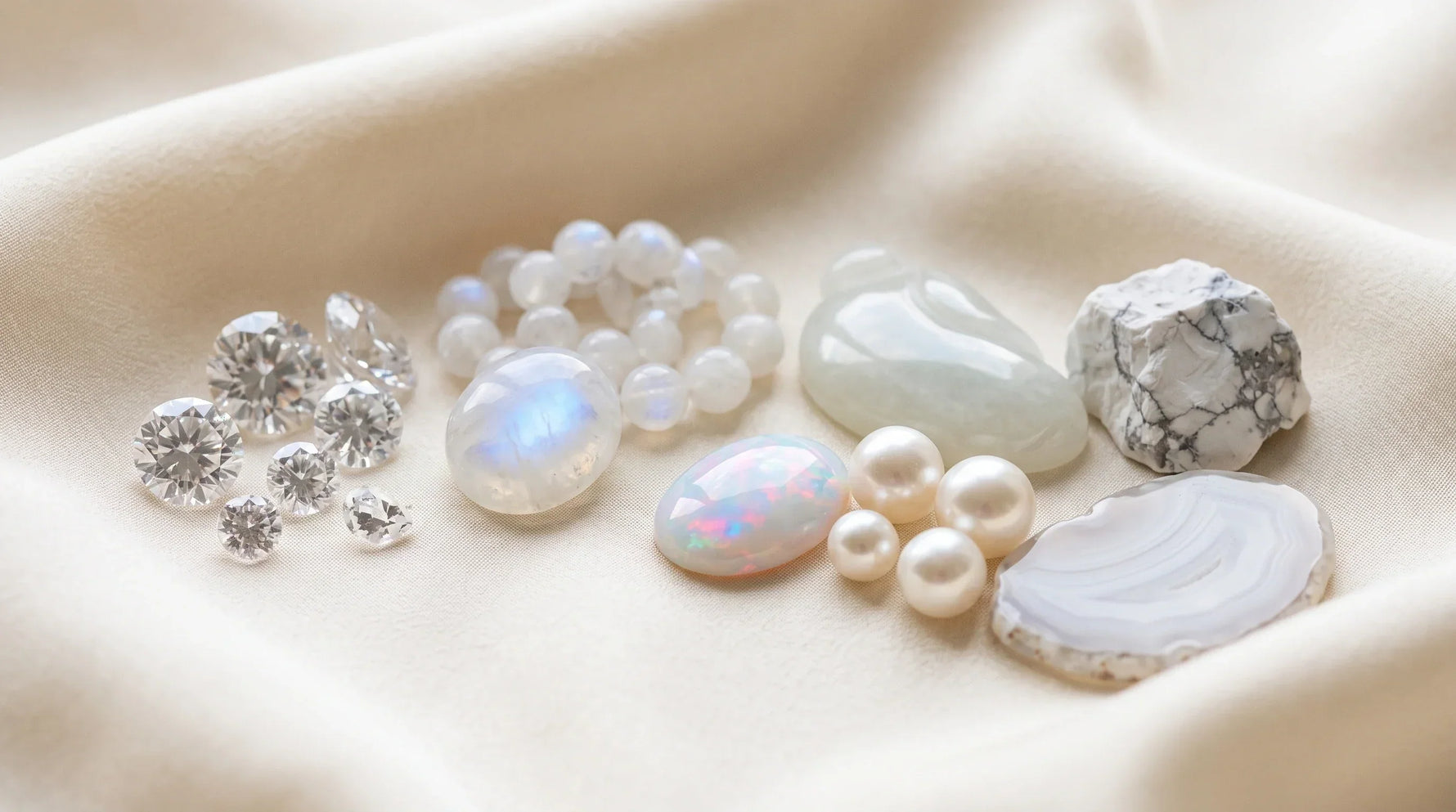 Different types of white gemstones arranged on ivory fabric, including clear, milky, and opaque white stones
